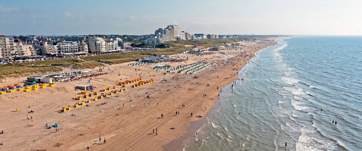 A coastal beach with people, buildings, and a clear sky.
