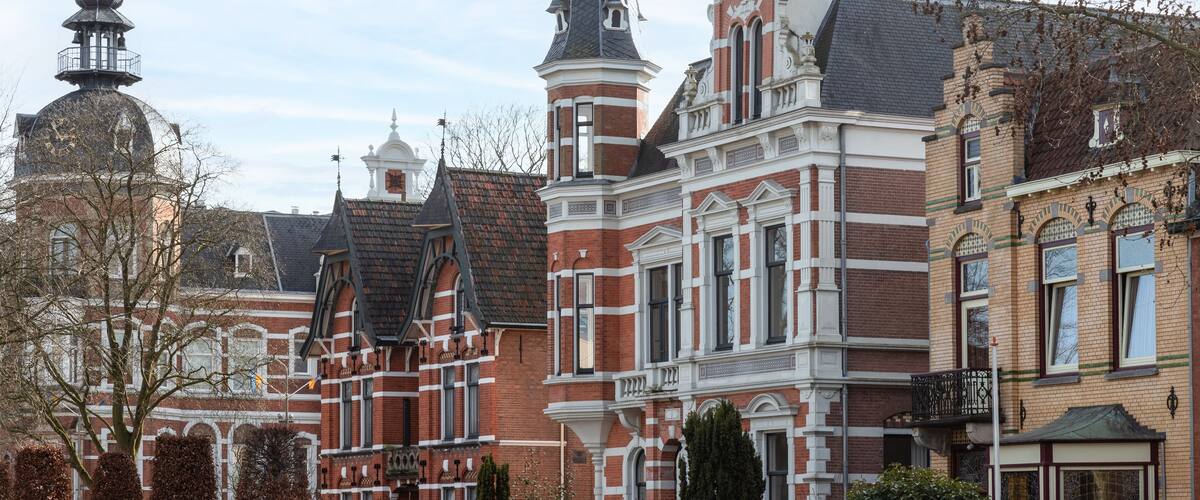 A historic building with red brick and white trim, a tower with a dome, and a large window with a balcony.
