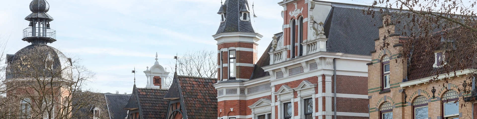 A historic building with red brick and white trim, a tower with a dome, and a large window with a balcony.