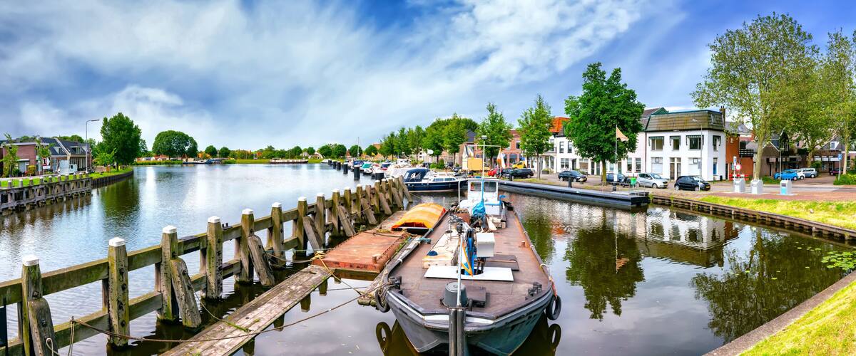 A canal with a wooden dock, boats, and a cityscape with buildings and trees.