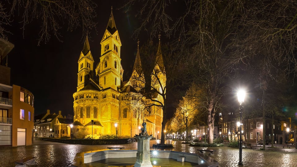 A historic church with multiple spires, illuminated at night, surrounded by cobblestone streets and trees.
