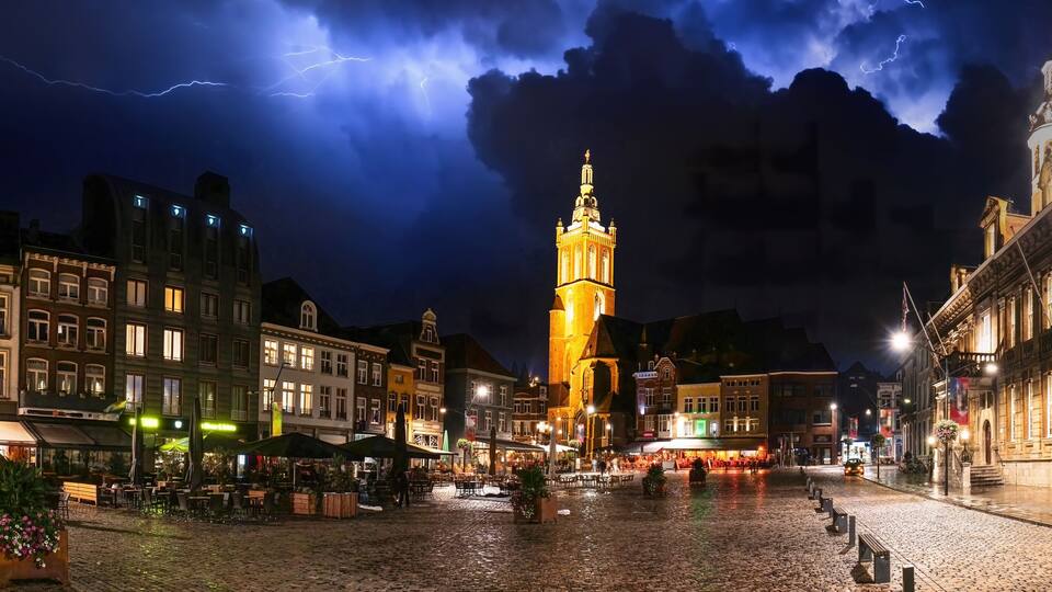 A historic square with cobblestone pavement, a prominent tower, and surrounding buildings with illuminated facades.