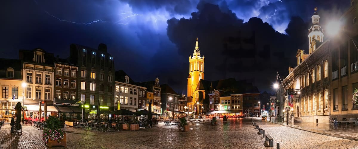 A historic square with cobblestone pavement, a prominent tower, and surrounding buildings with illuminated facades.