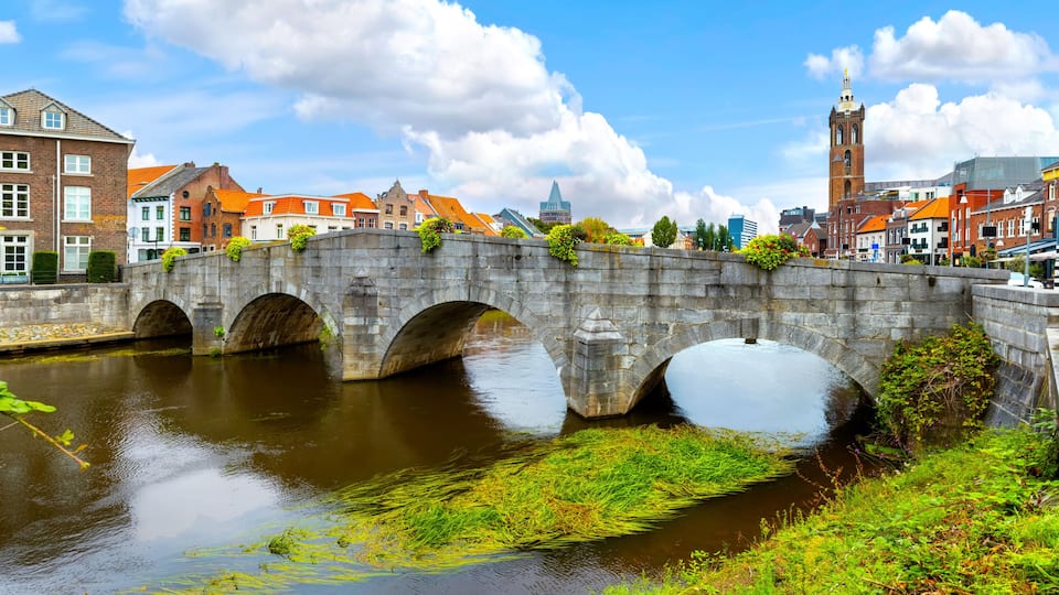 A stone bridge over a river with buildings and a tower in the background.
