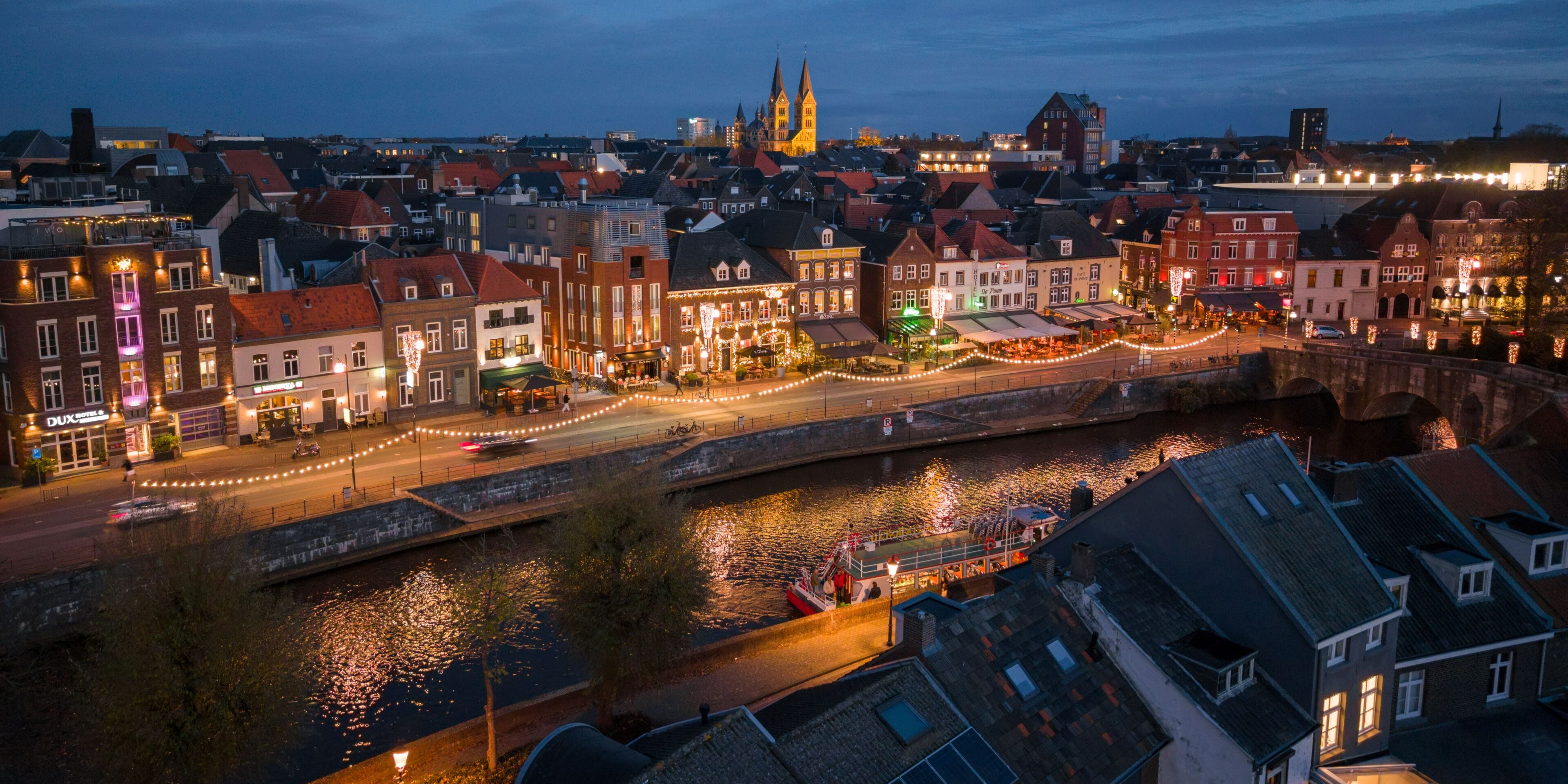 Aerial view of a canal reflecting the warm glow of evening lights along buildings and the Sint Christoffelkathedraal, Roermond, Limburg, Netherlands.