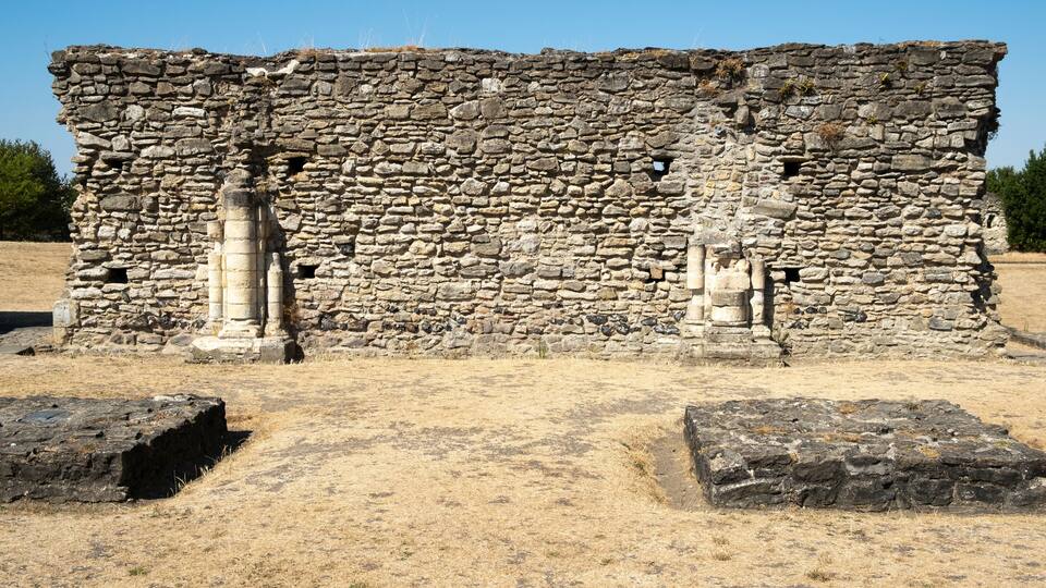 An ancient stone structure with columns and a dry, grassy field.