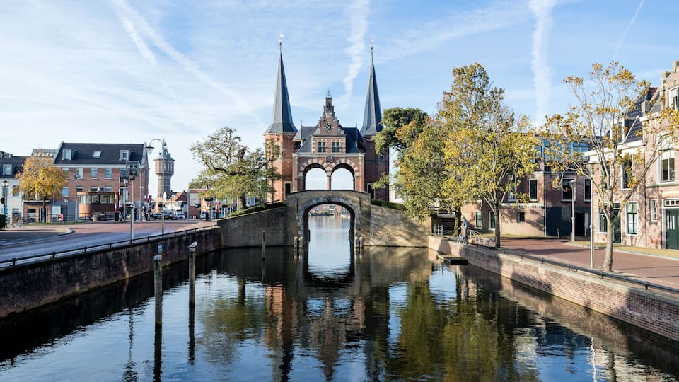 A canal with a bridge and a church with two spires.