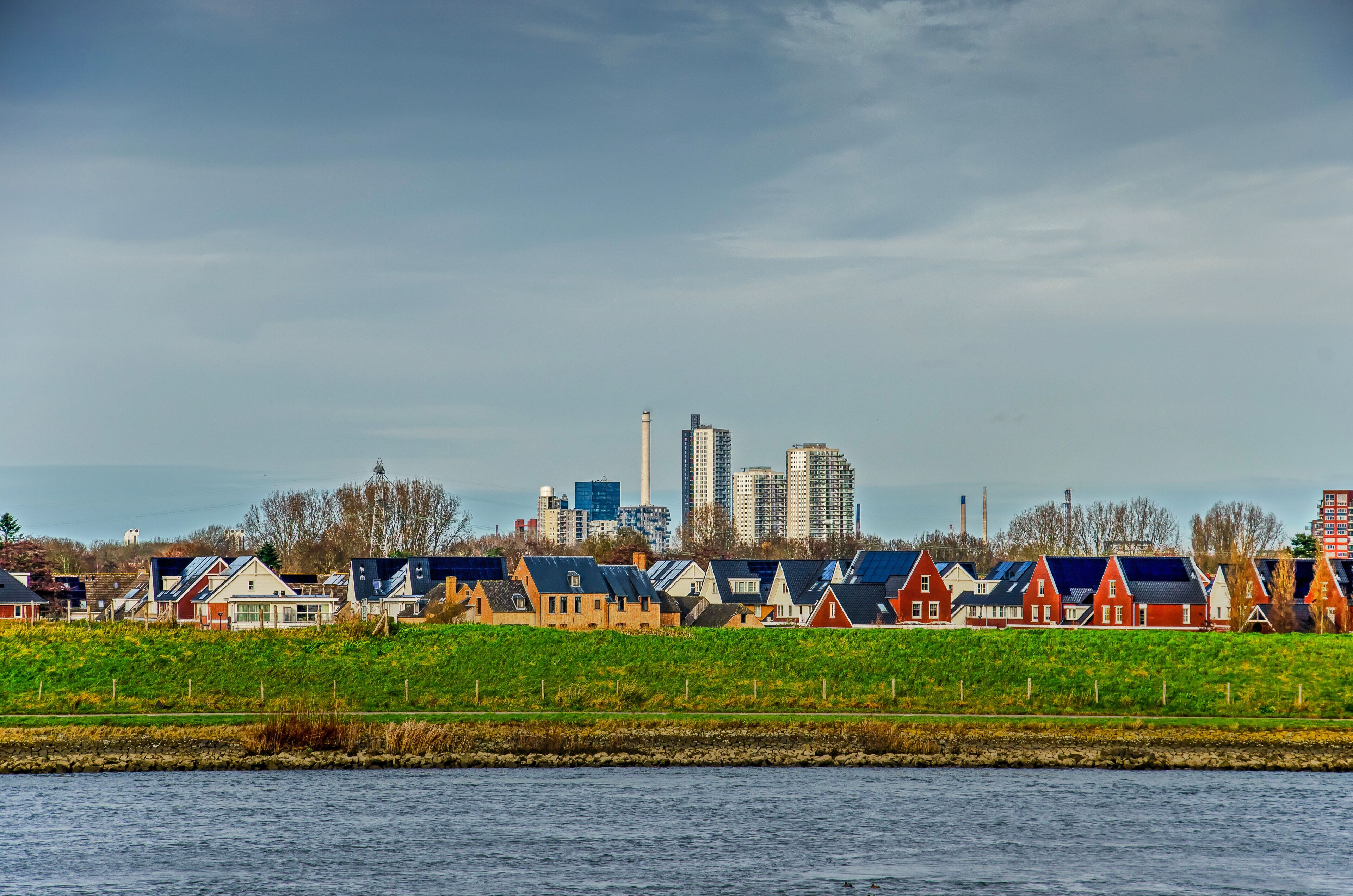 Un paisaje marítimo con casas rojas, el horizonte de una ciudad y una extensión de agua.