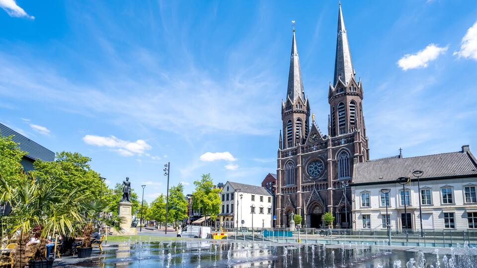 A historic church with twin spires, a fountain, and surrounding buildings.