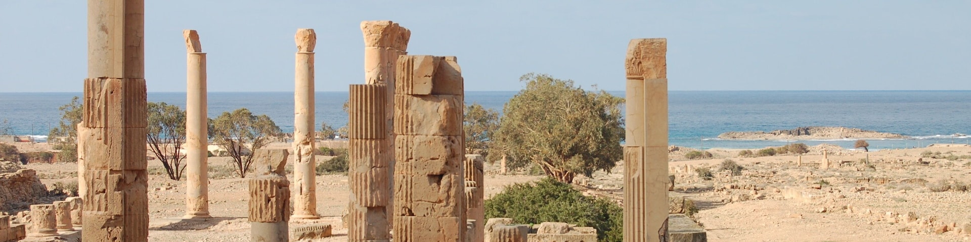 Ancient ruins with columns and a view of the sea.