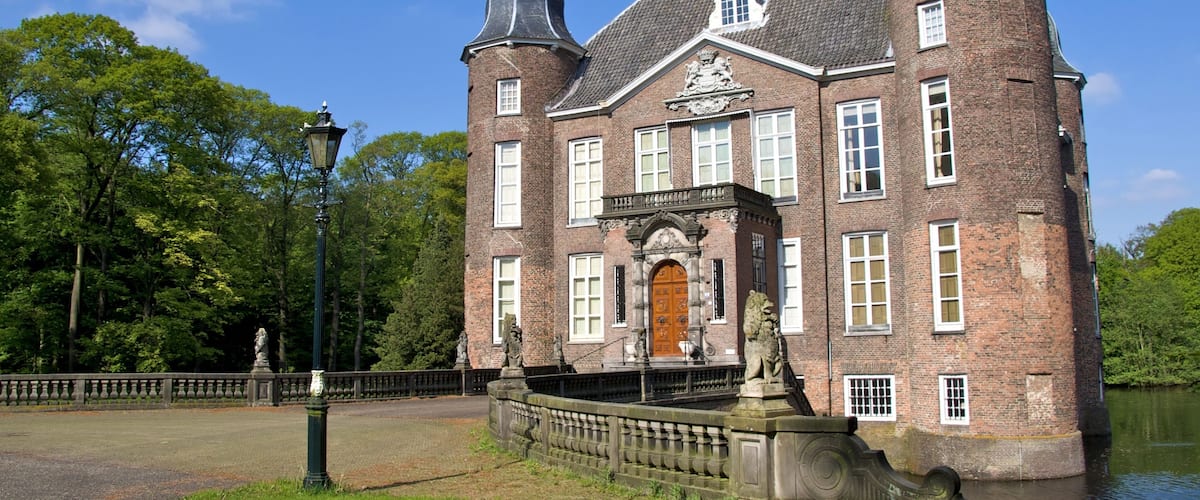 A historic brick building with a large wooden door, surrounded by a moat and a stone bridge.