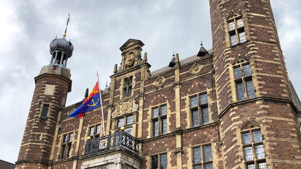 A historic building with two towers, a central entrance, and flags.