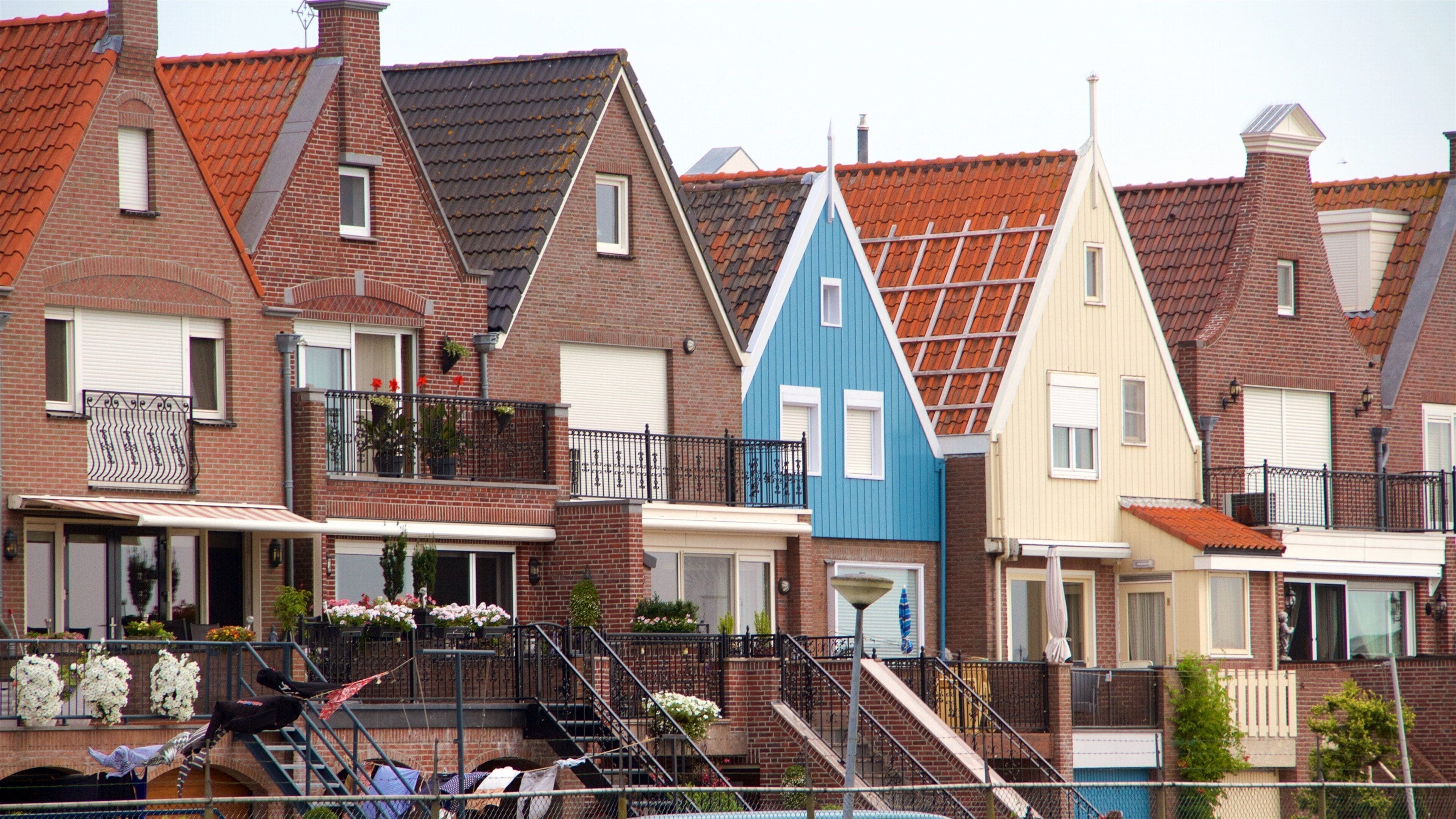 A row of colorful houses with red, blue, and cream facades, red-tiled roofs, and brick construction.
