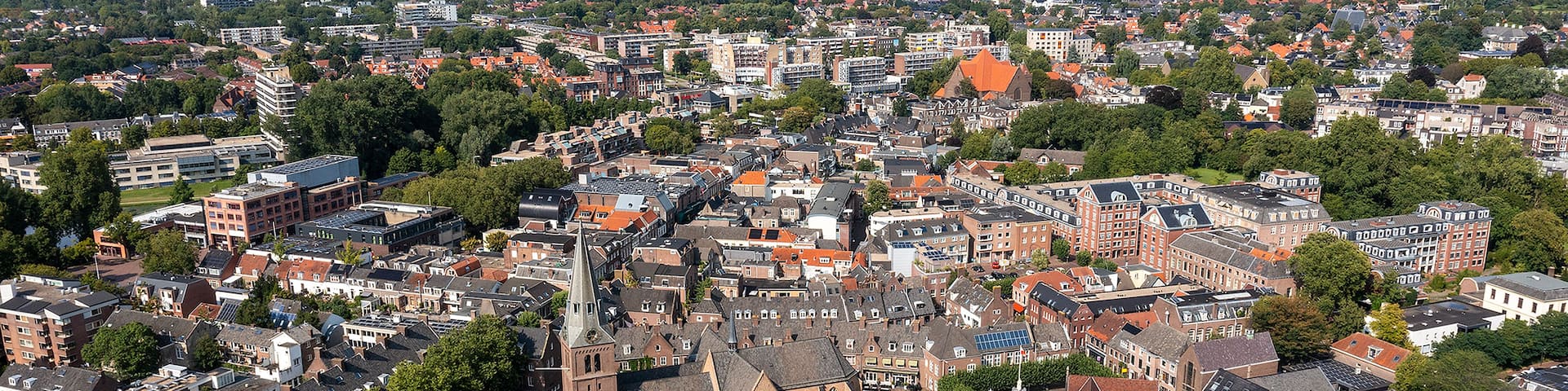 A densely built urban area with historic architecture, including a prominent church with a tall steeple, surrounded by residential buildings and greenery.