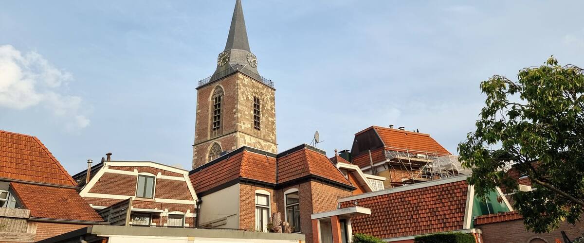 A church with a tall steeple and a clock, surrounded by residential buildings with red roofs.