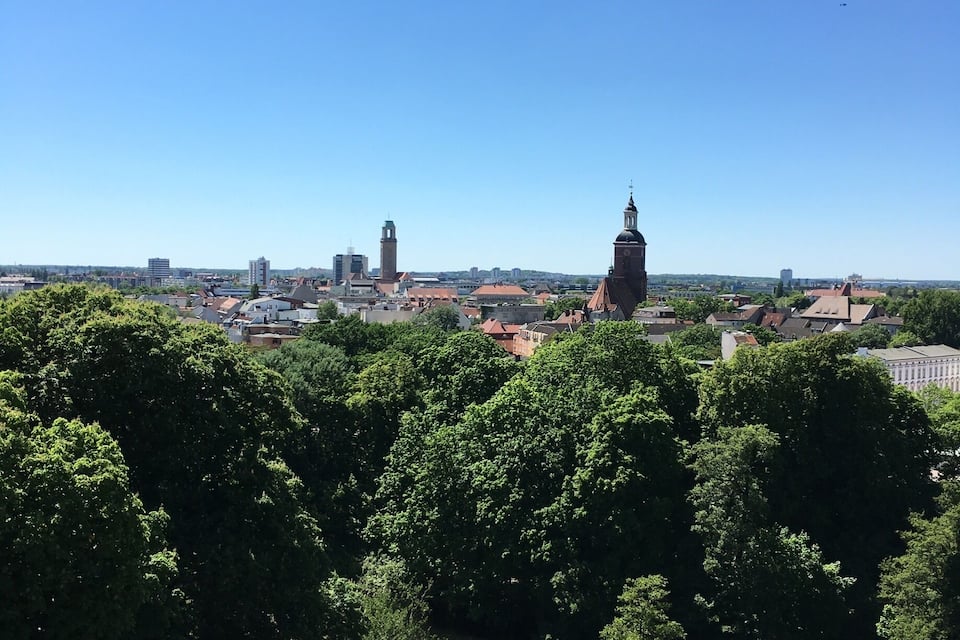 A cityscape with a prominent tower, lush green trees, and a clear blue sky.