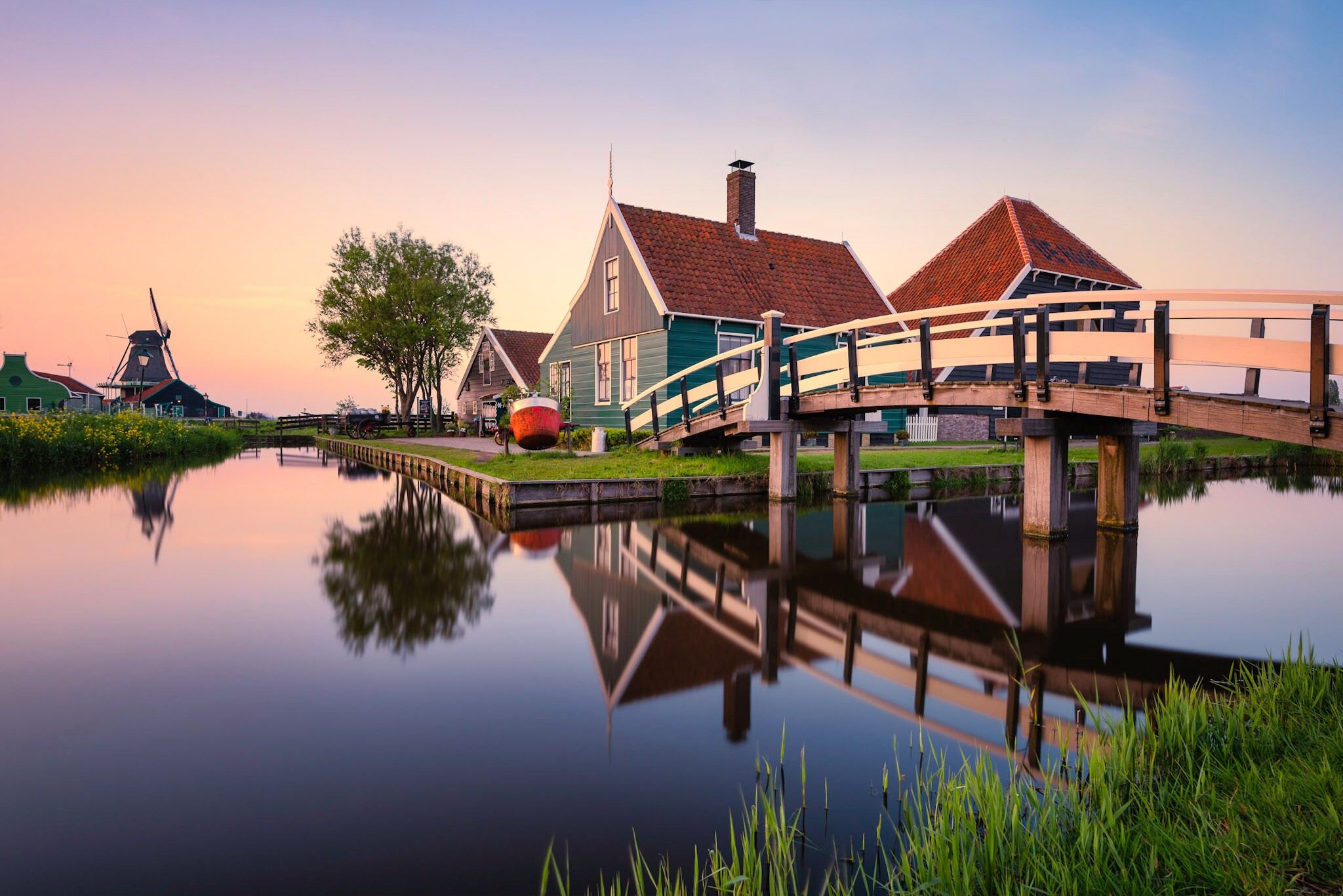 A canal with a wooden bridge, traditional houses, and a windmill.