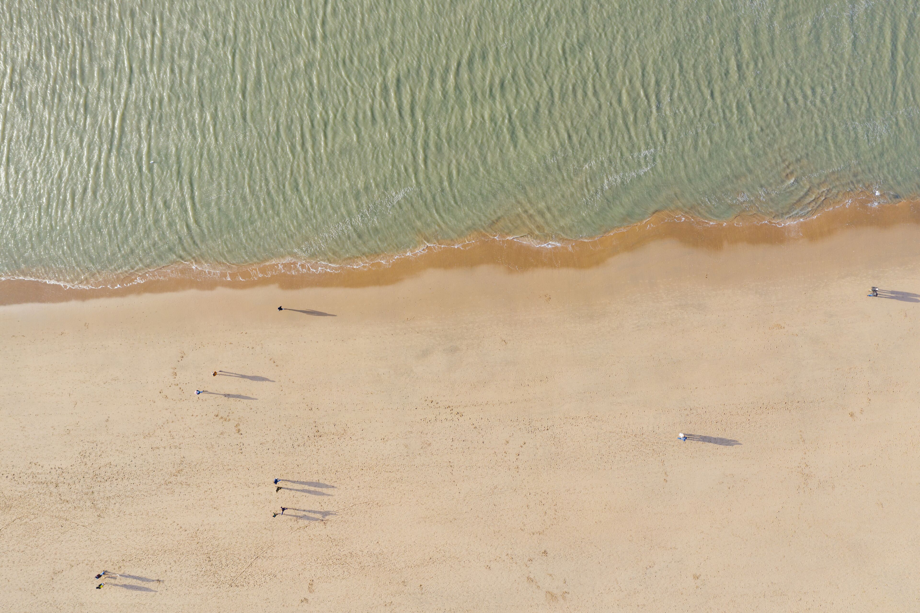 Uma praia arenosa com uma onda grande se aproximando e vários objetos pequenos espalhados na areia.