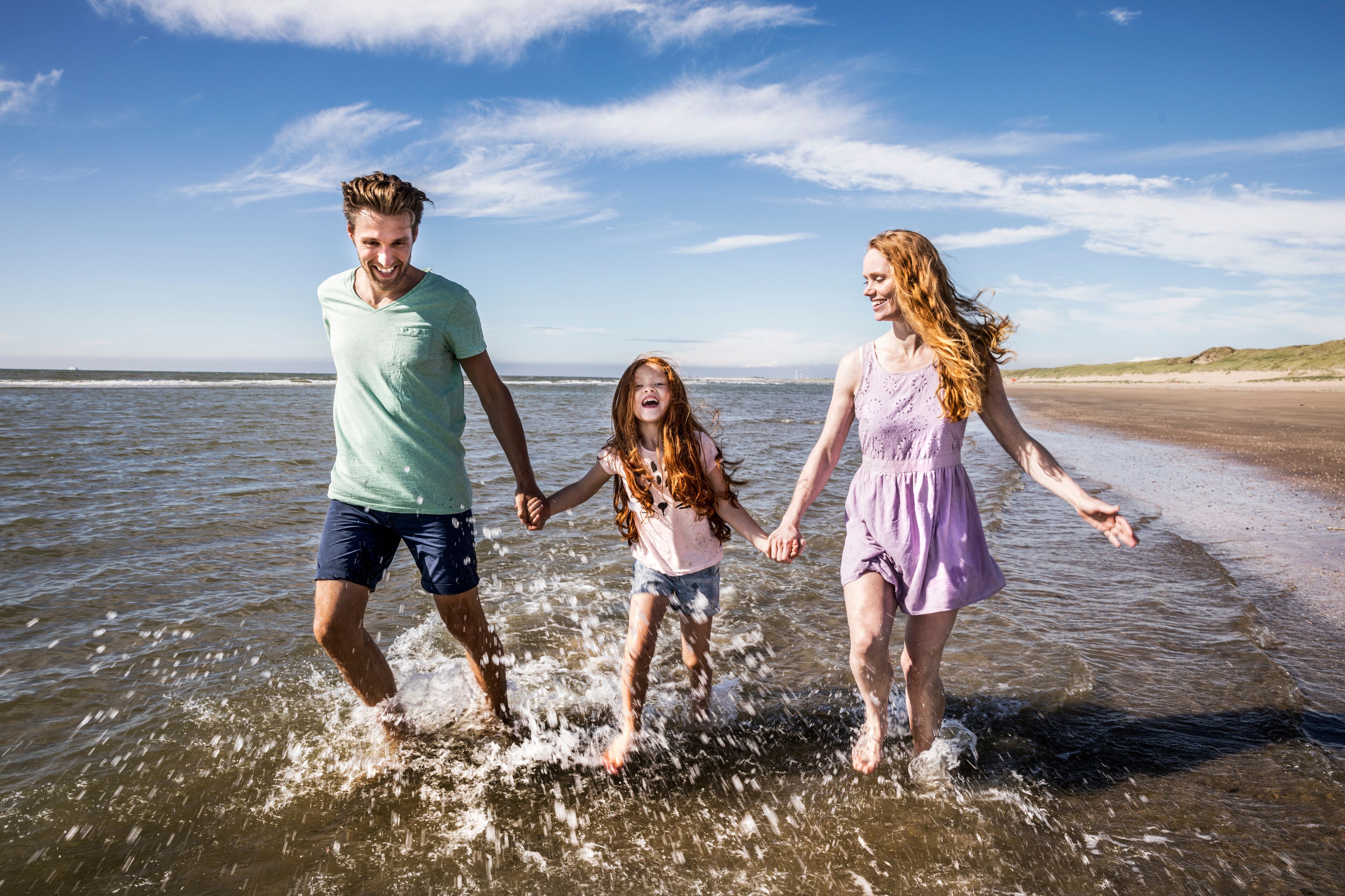 A family walking on a beach with water up to their ankles.