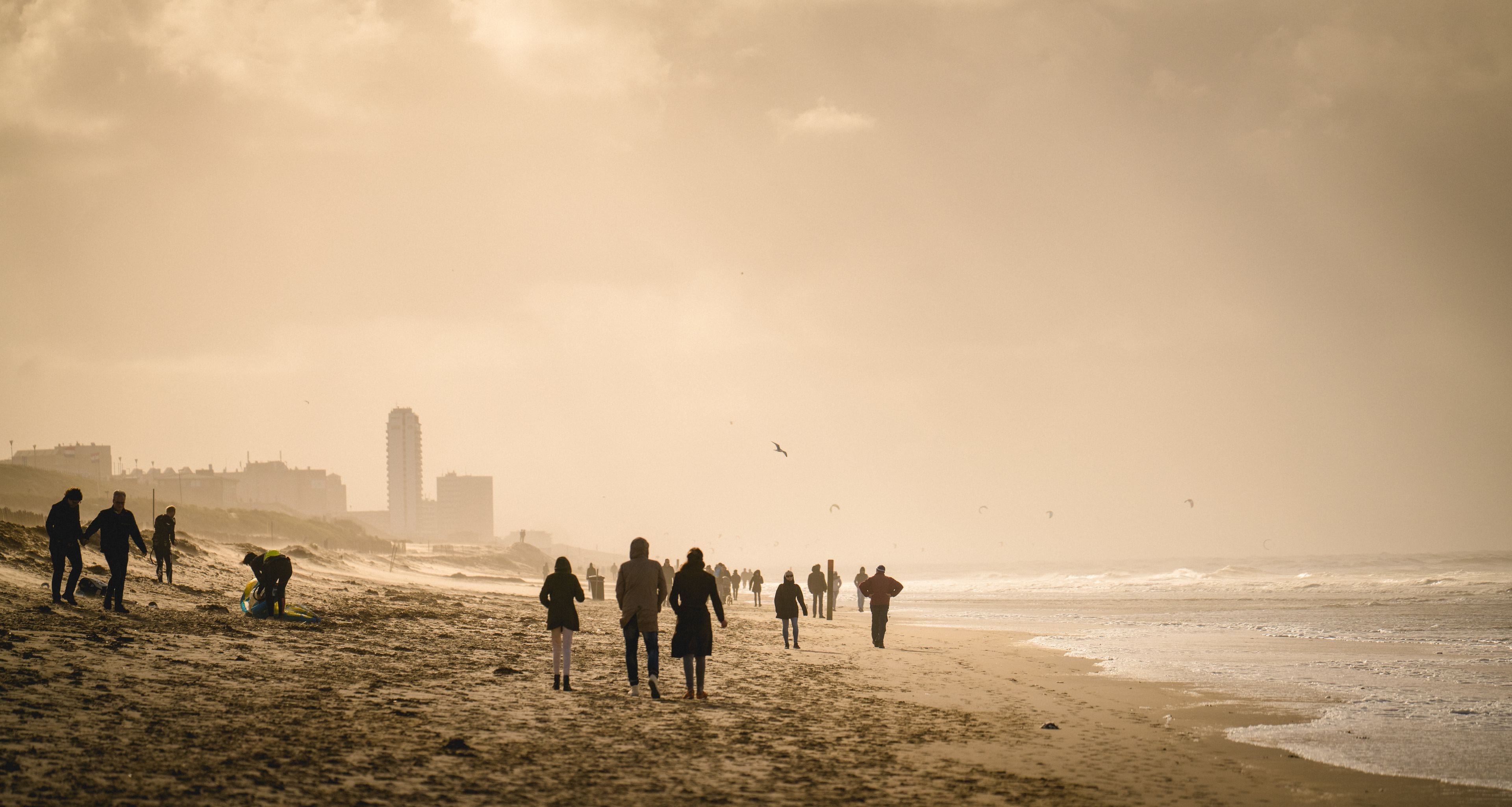 A beach with people walking, waves crashing, and a distant building.