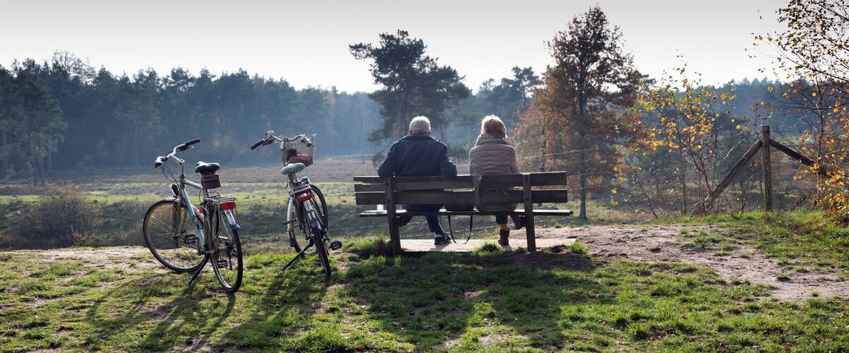 A couple sitting on a bench overlooking a grassy field with bicycles parked nearby.