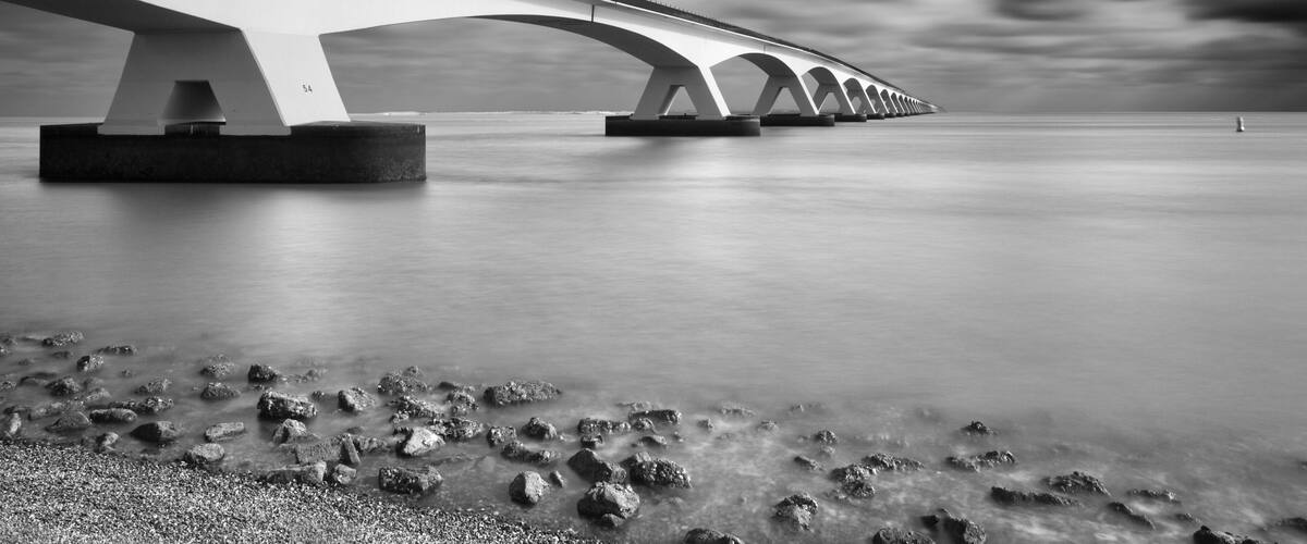 Een brug over kalm water met een rotsachtige oever.