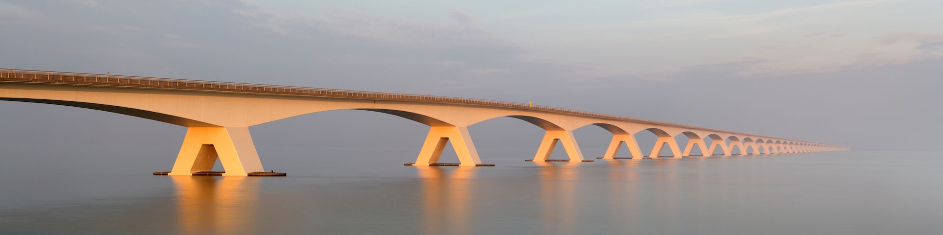 A long bridge with multiple arches spanning a calm body of water.
