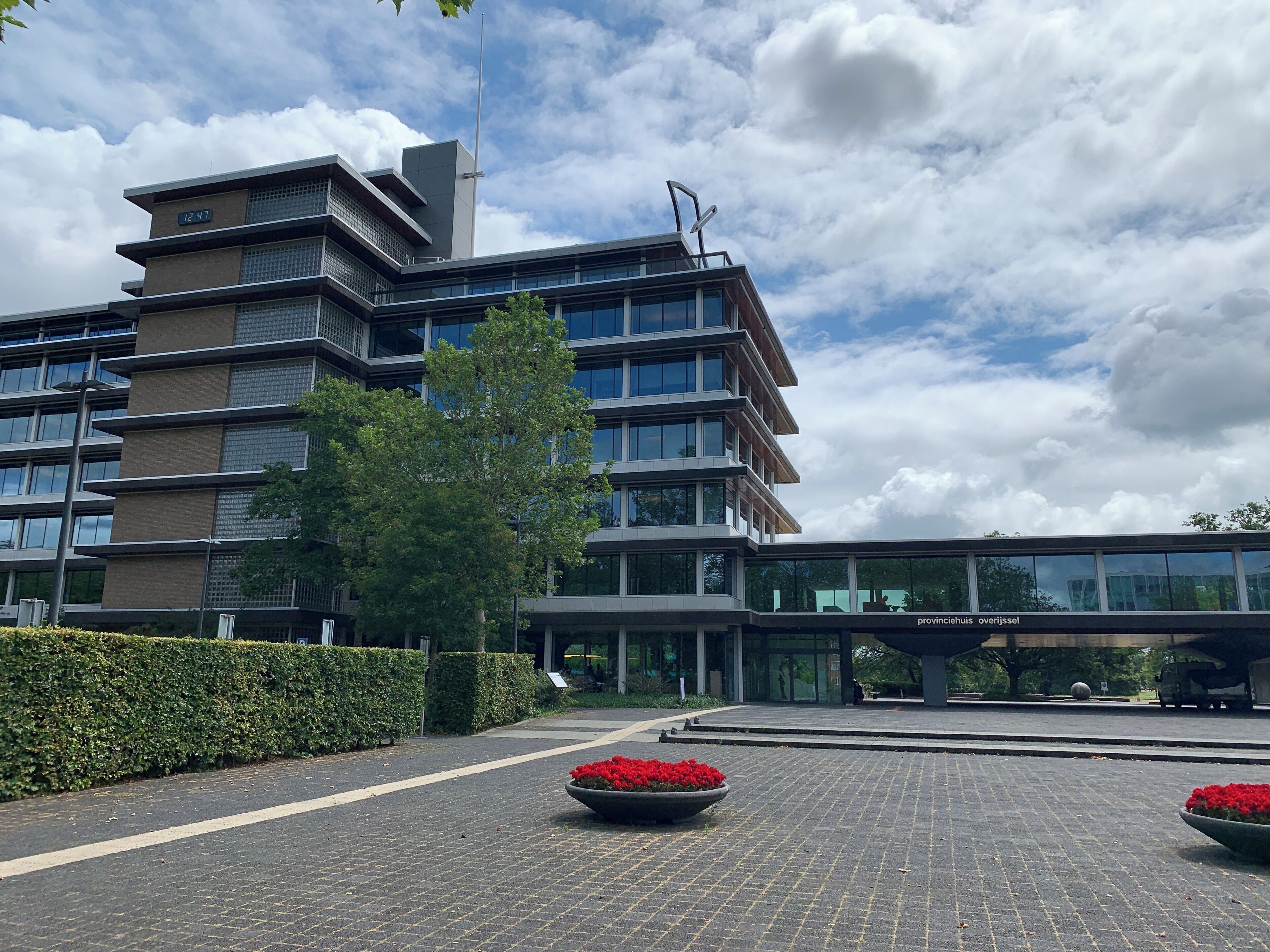 A modern building with a digital clock, a tree, and red flower planters.