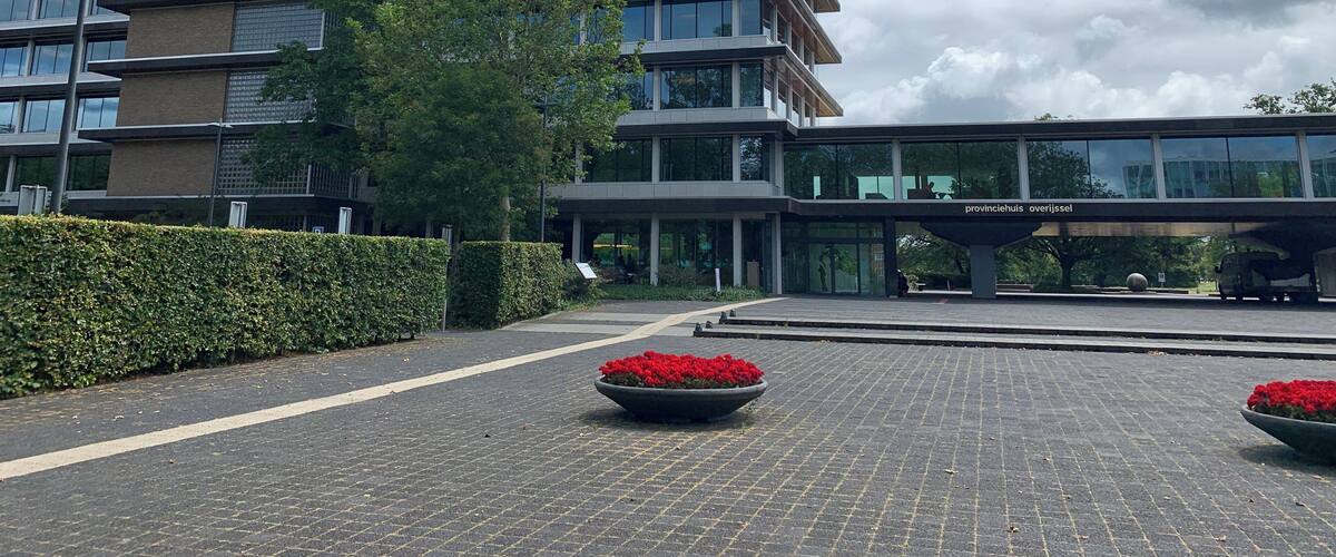 A modern building with a digital clock, a tree, and red flower planters.