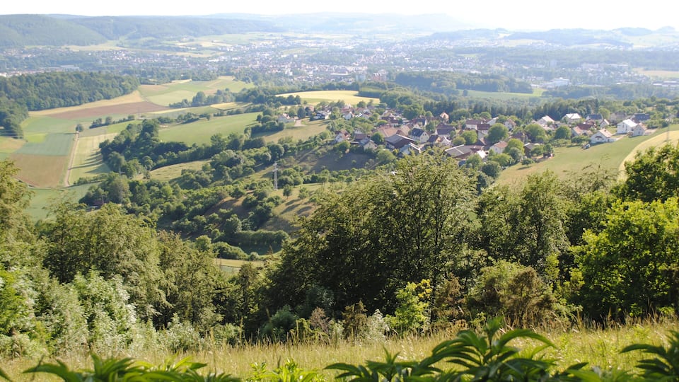 A rural landscape with rolling hills, scattered houses, and dense forests.