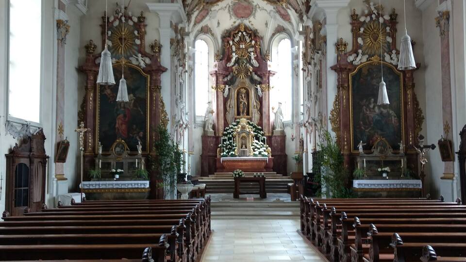 An ornate church interior with a central altar, pews, and detailed frescoes on the ceiling.