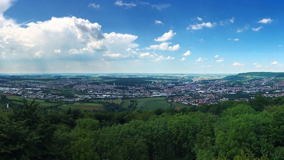 A panoramic view of a town nestled in a valley with lush greenery and rolling hills in the background.