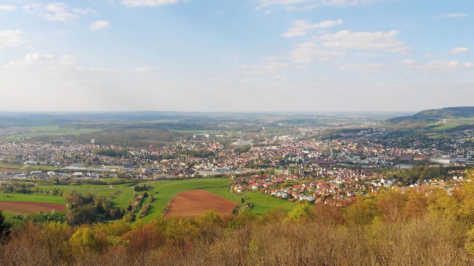 A panoramic view of a town nestled in a valley with rolling hills in the background.