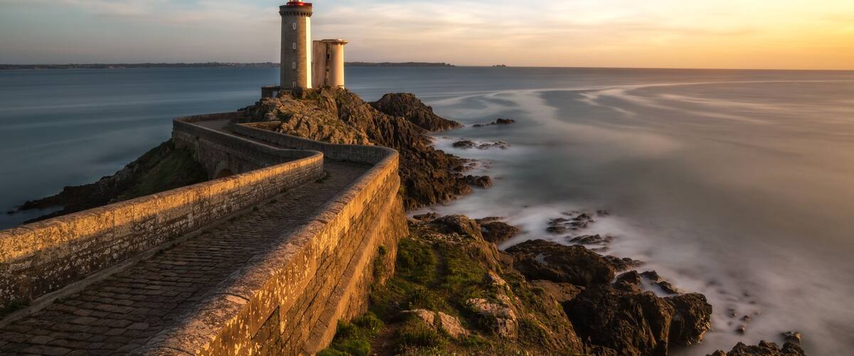 A coastal lighthouse, a stone staircase, and a calm sea with a long exposure effect.