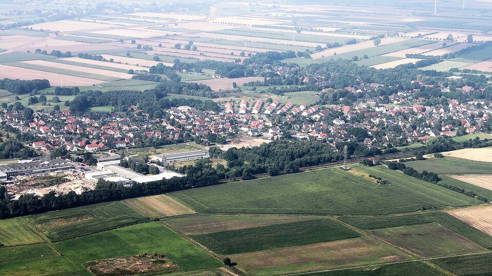 An aerial view of a rural town with fields, houses, and wind turbines.