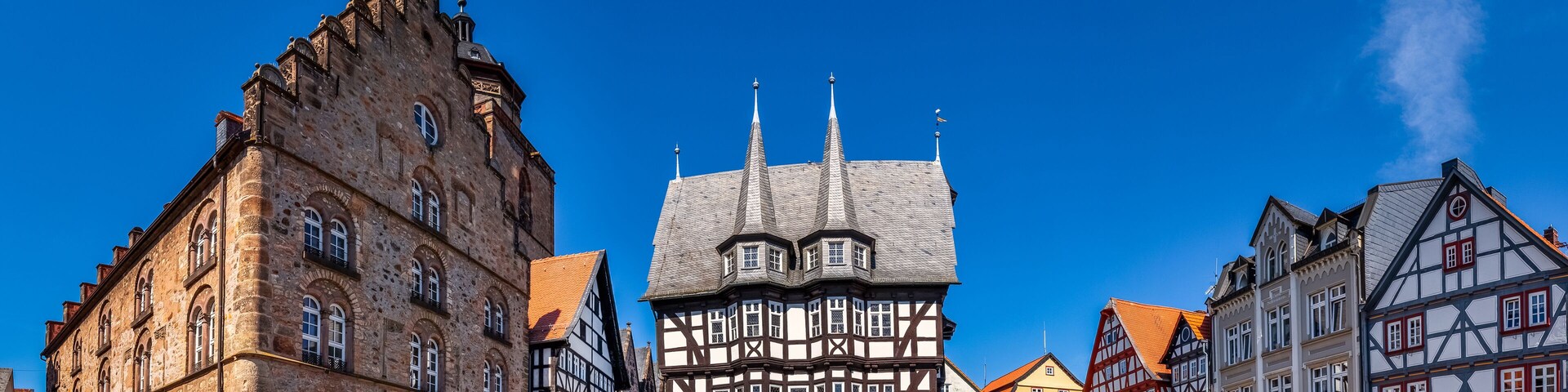 A historic town square with medieval buildings, including a prominent church with a spire.