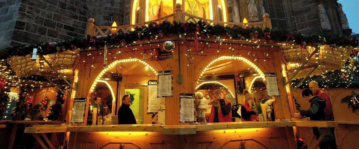 A traditional wooden Christmas market stall with a star-shaped lantern, set against a historic stone building with a tower.