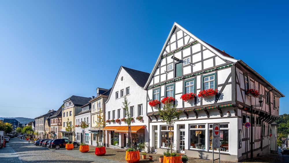 A cobblestone street lined with traditional half-timbered buildings, some with red flower boxes.