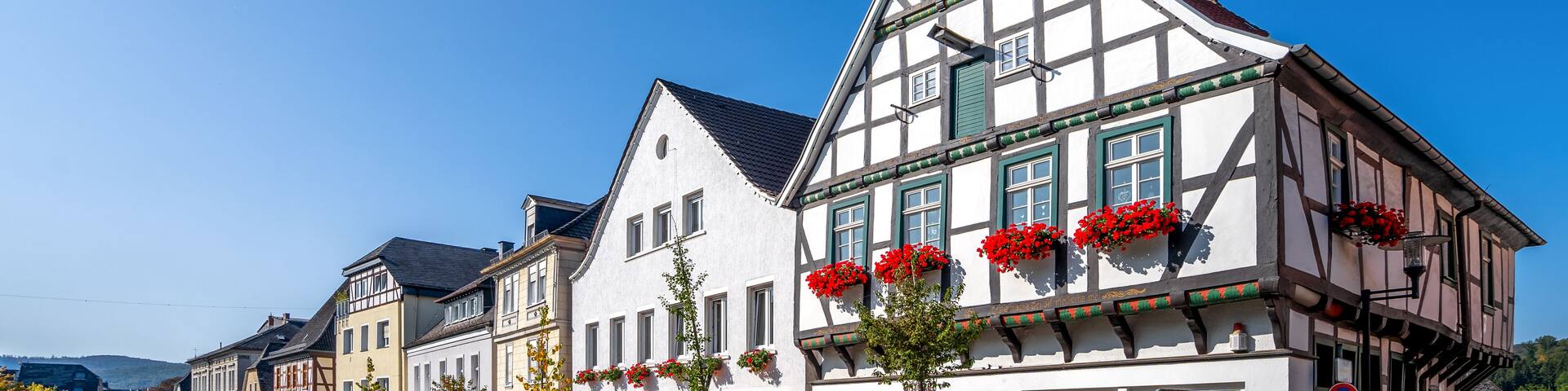 A cobblestone street lined with traditional half-timbered buildings, some with red flower boxes.