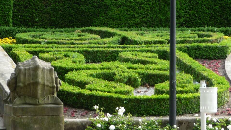 A formal garden with neatly trimmed hedges, a stone statue, and a lamppost.