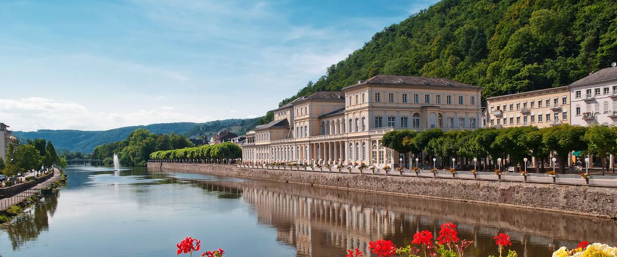 A river with a bridge, a row of buildings, and a hillside.