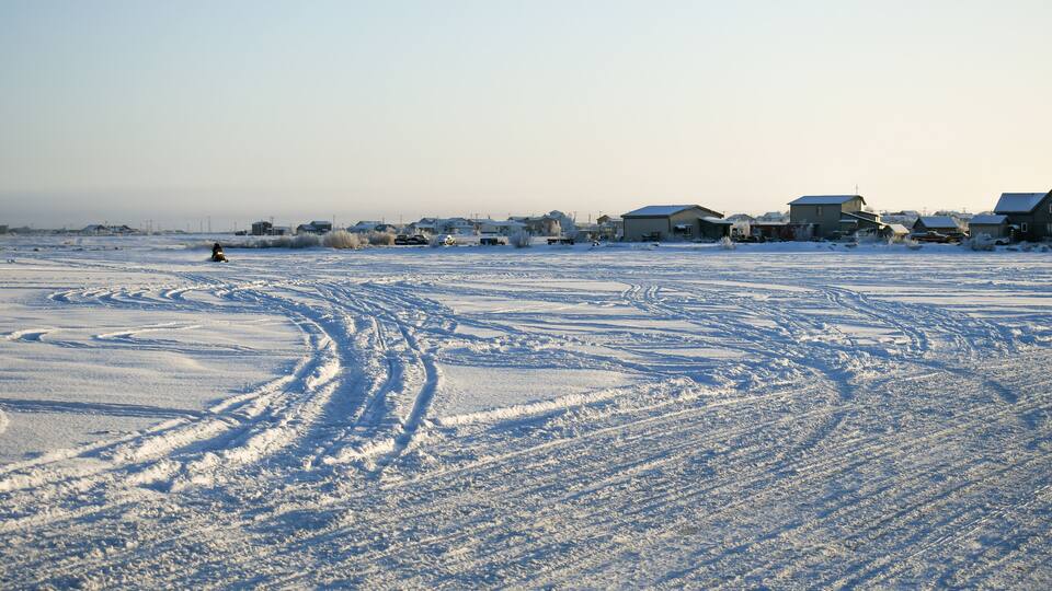 A snowy landscape with houses and tire tracks.