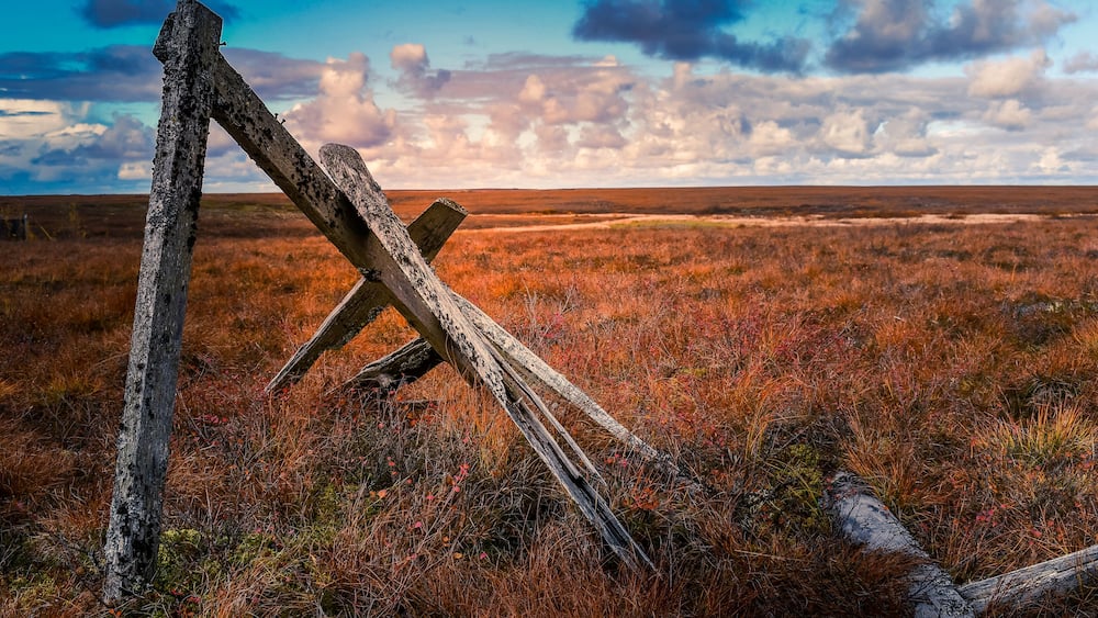 A fallen wooden fence in a grassy field with a cloudy sky.