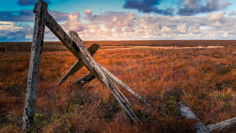 A fallen wooden fence in a grassy field with a cloudy sky.