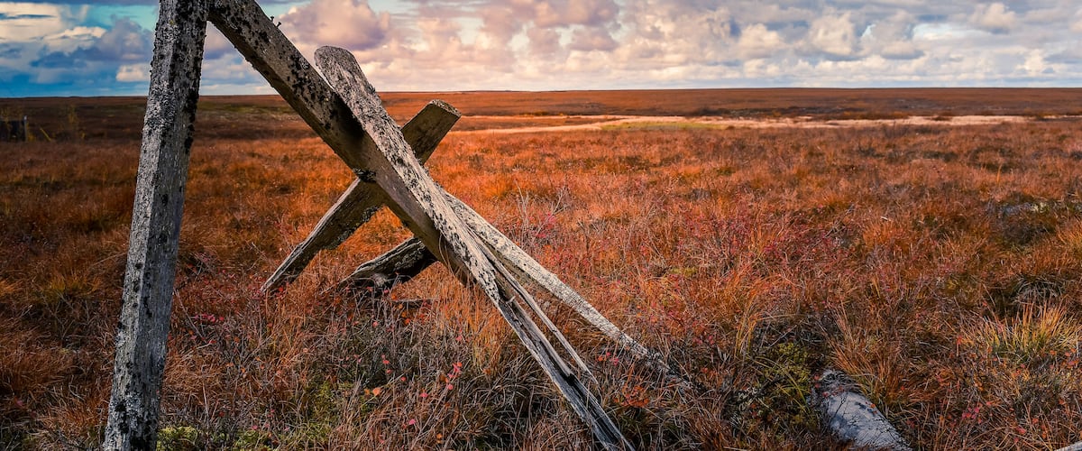 A fallen wooden fence in a grassy field with a cloudy sky.