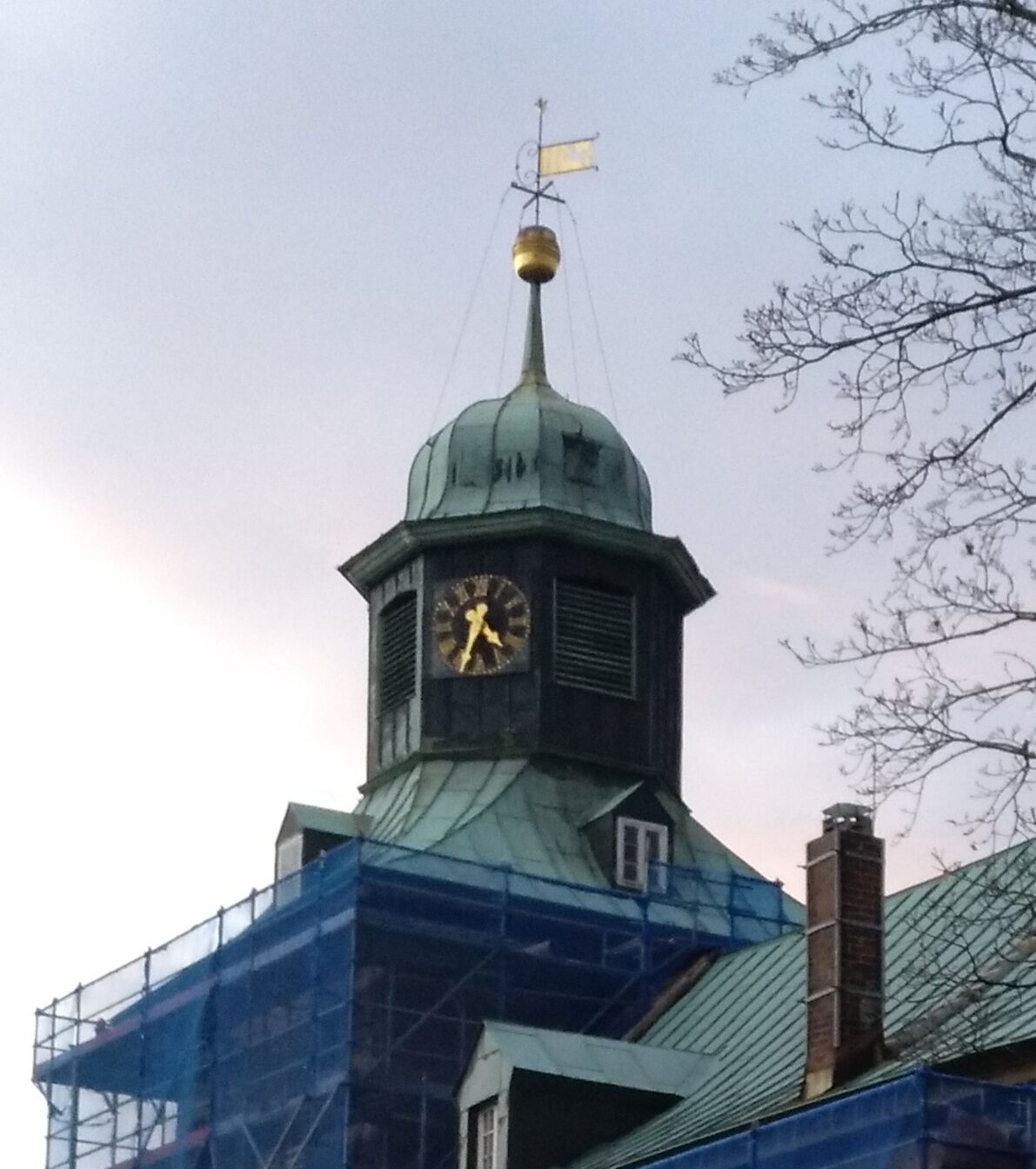 A clock tower with a weather vane and a dome, surrounded by scaffolding.