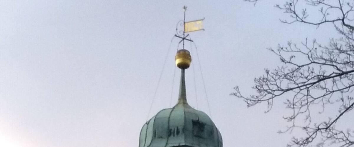 A clock tower with a weather vane and a dome, surrounded by scaffolding.