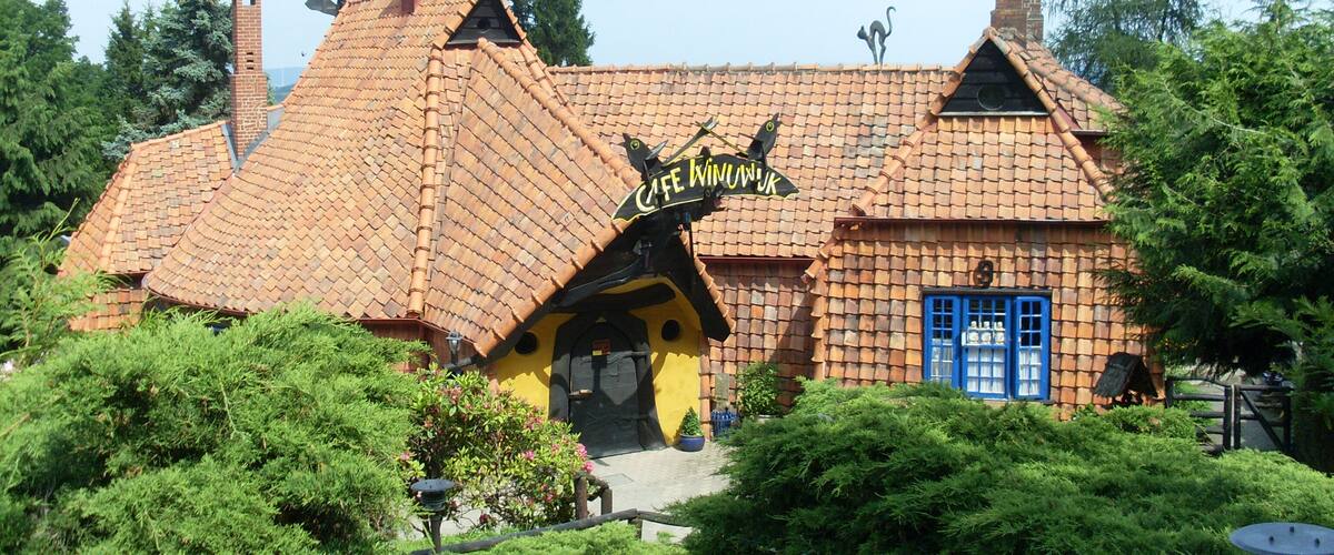 Une maison fantaisiste, dotée d’un toit à forte pente, d’une cheminée et d’une enseigne sur laquelle on peut lire « Café Winiewka ».