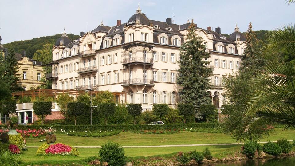 A large, ornate building with multiple balconies and a garden with a pond.