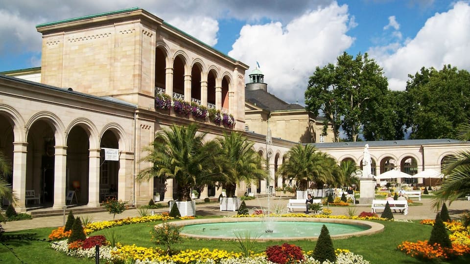 A historic building with arched windows and a fountain surrounded by a garden.